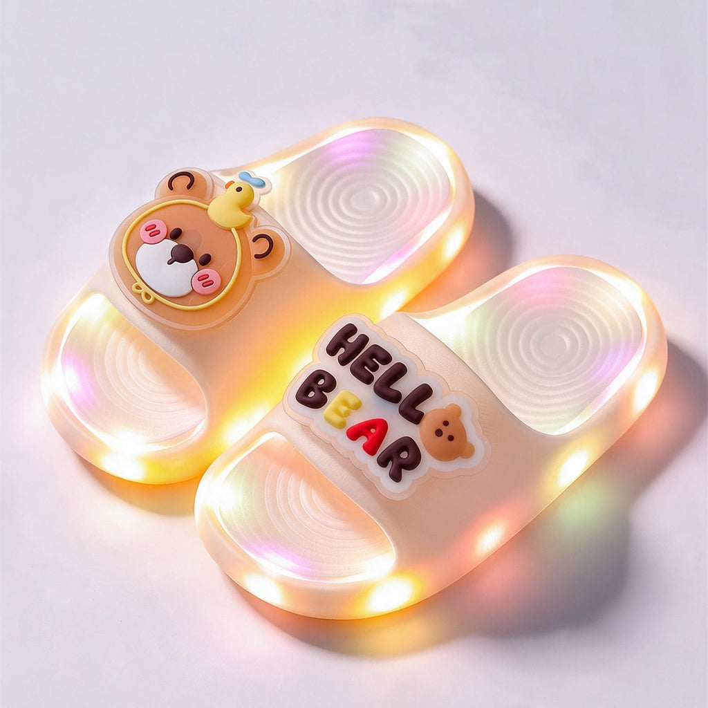 A pair of cream Hello Bear STEPGLO slides, one strap with a bear face and the other with HELLO BEAR in raised letters, LEDs lit around both soles.